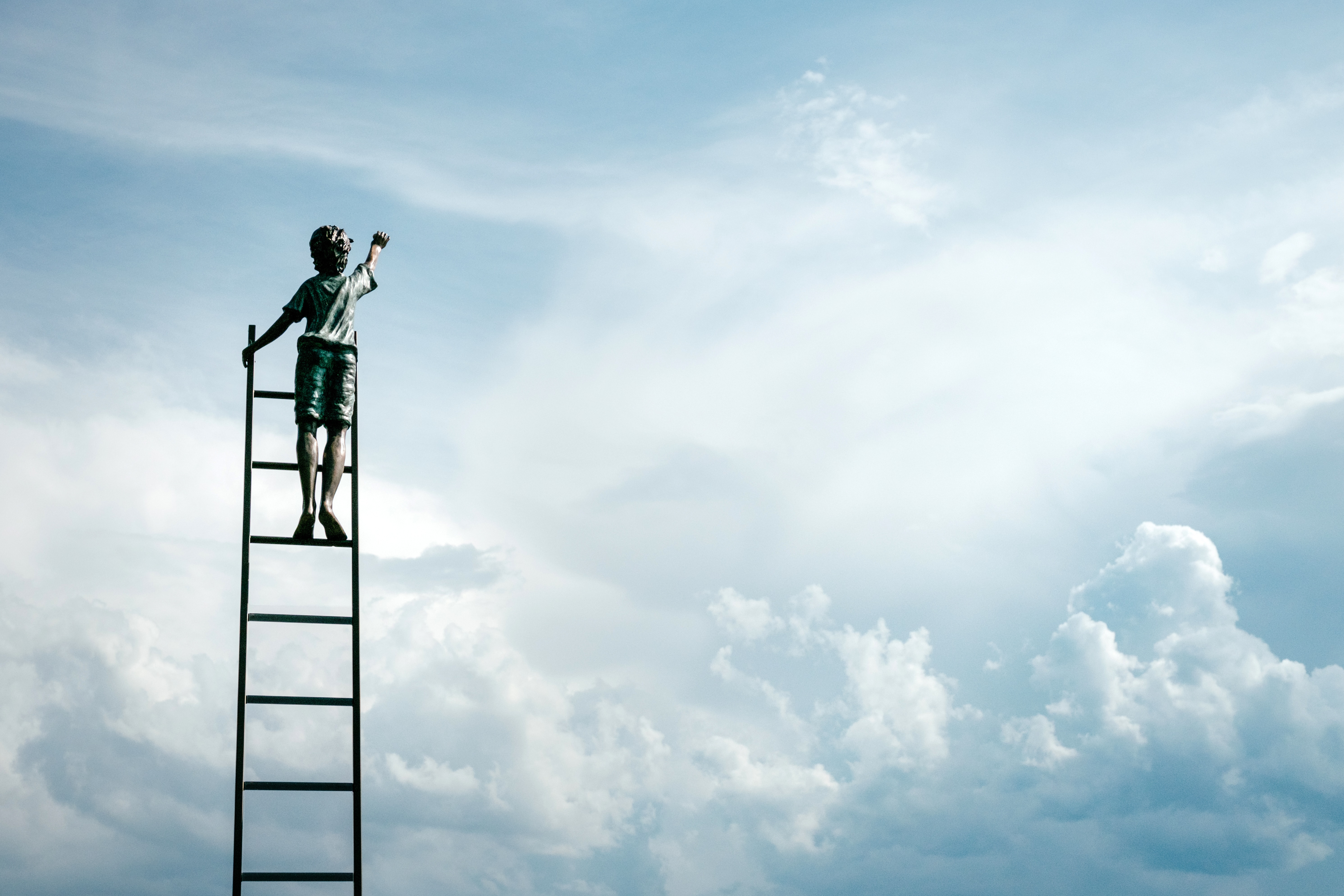 Boy at top of ladder reaching for the sky